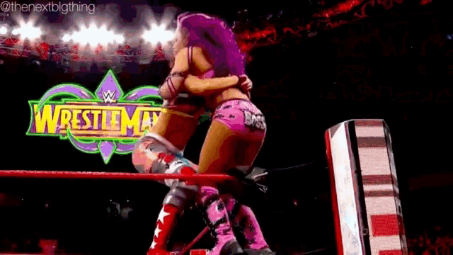two women are hugging in a wrestling ring with a wrestlemania sign in the background