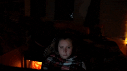 a girl wrapped in a plaid blanket is looking at a screen in the dark