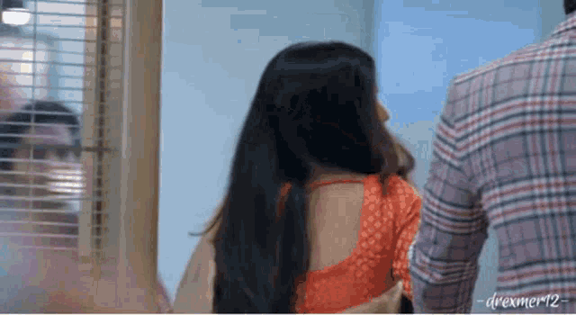 a man in a plaid shirt is standing next to a woman in an orange blouse .