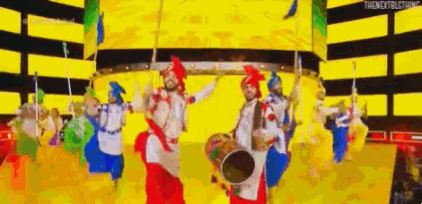 a group of people are dancing and playing drums on a stage in front of a yellow background .