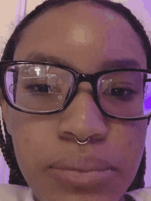 a woman wearing glasses and a nose ring is looking at the camera