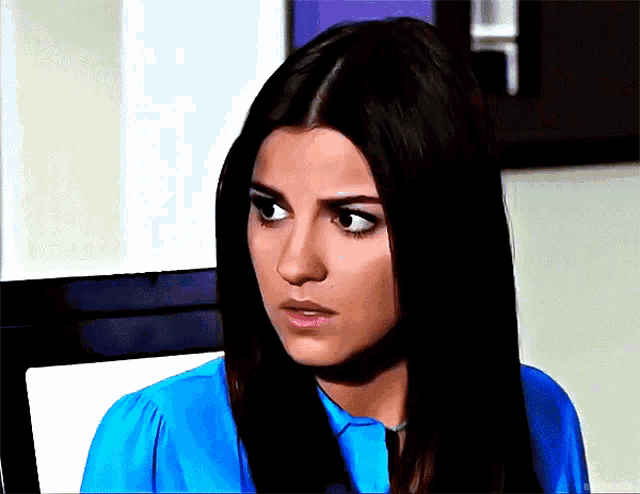 a woman in a blue shirt looks at the camera with a surprised look on her face