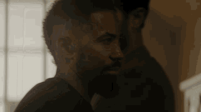 a man with a beard is standing next to another man in a dark room