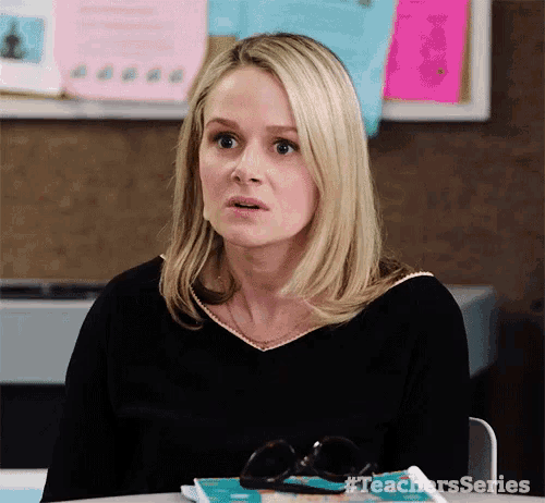 a woman is sitting at a desk in front of a bulletin board with sticky notes .
