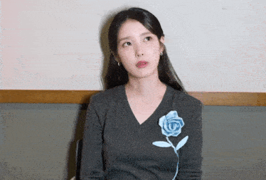 a woman wearing a gray sweater with a blue flower on her chest