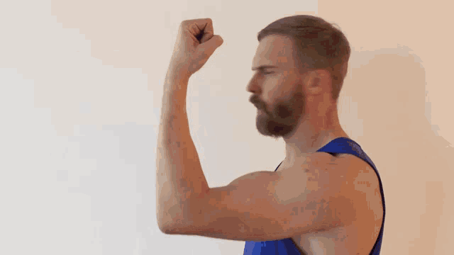 a man in a blue tank top holds his fist up in front of a white wall with the word uh written on it