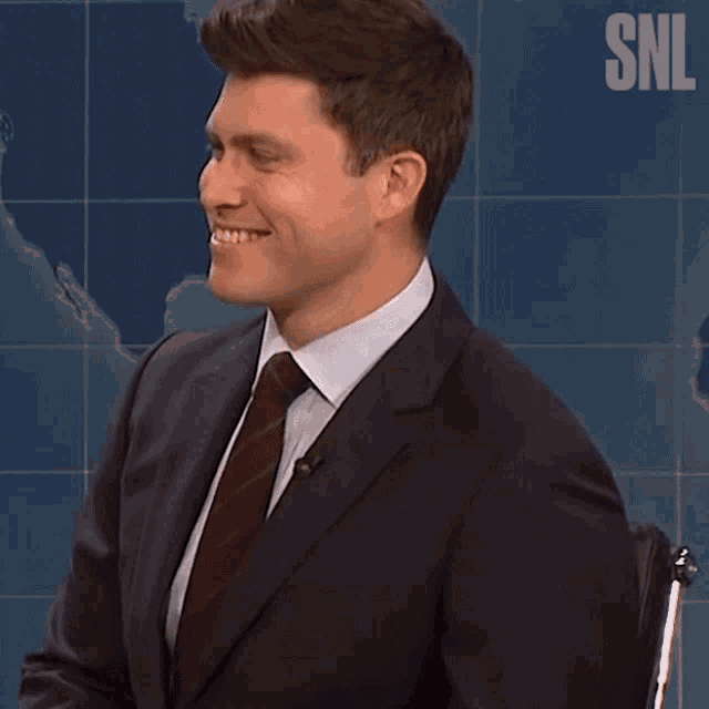 a man in a suit and tie is smiling in front of a snl sign