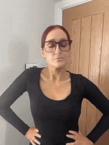 a woman wearing glasses and hoop earrings is standing in front of a wooden door