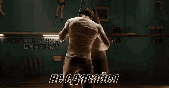 a man in a white shirt is punching a punching bag in a dark room with russian writing on it .