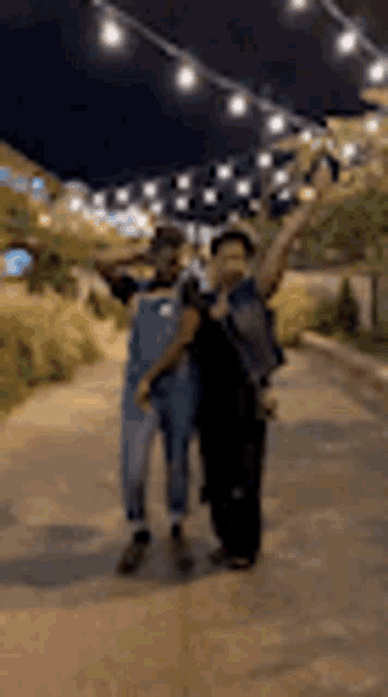 a couple of people standing next to each other on a sidewalk at night .