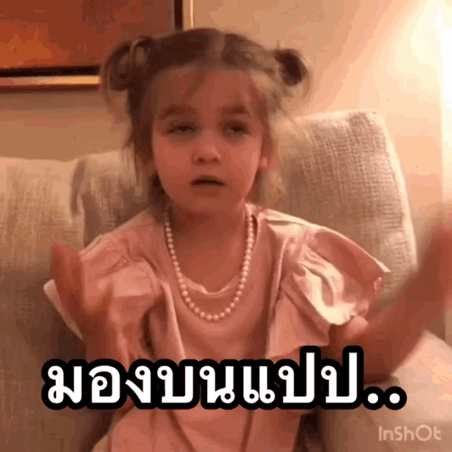 a little girl wearing a pearl necklace is sitting on a couch with her hands in the air