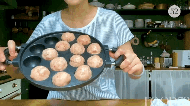 a woman is holding a pan of meatballs with the number 52 on the bottom right