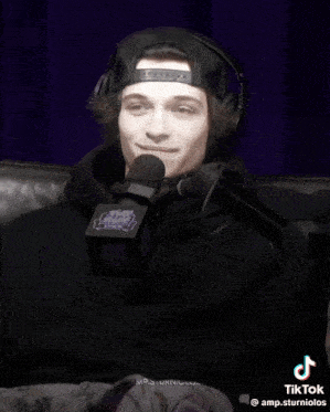 a man wearing headphones and a hat is sitting in front of a microphone that says amp.sturniolos