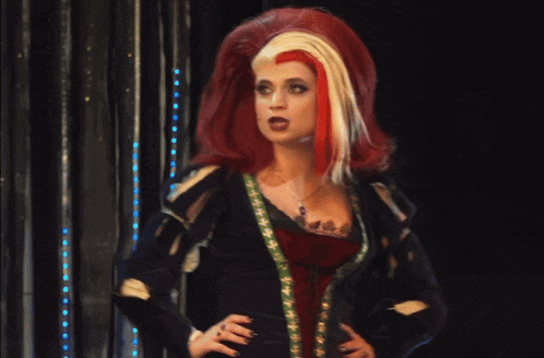 a woman with red hair and white hair is standing with her hands on her hips in a dark room