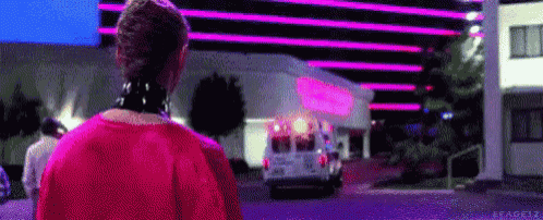 a woman in a red dress is walking down a street in front of a building with ambulance in the background .