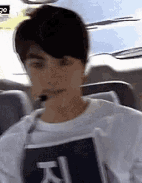 a young man is sitting in a car wearing a microphone and holding a sign .