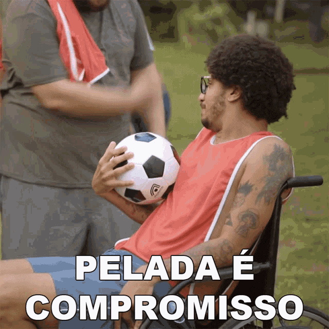 a man in a wheelchair holding a soccer ball with the words pelada e compromisso written below him