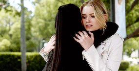 a woman in a white jacket is hugging another woman in a park .