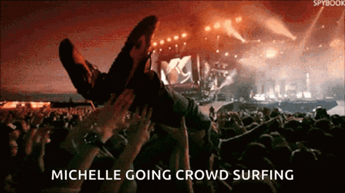 a crowd of people at a concert with the words michelle going crowd surfing below them