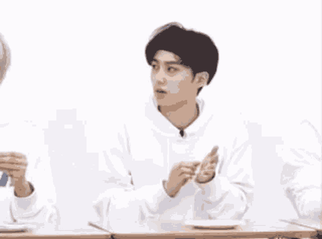 a young man in a white hoodie is sitting at a table with a plate of food .
