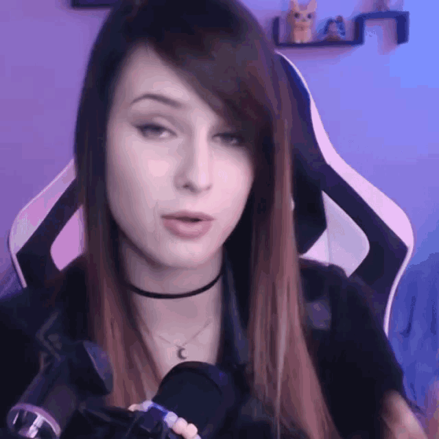 a woman is sitting in a gaming chair with a microphone in front of her .