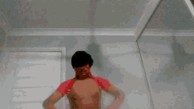 a shirtless man in a red shirt is standing in front of a mirror and giving the middle finger