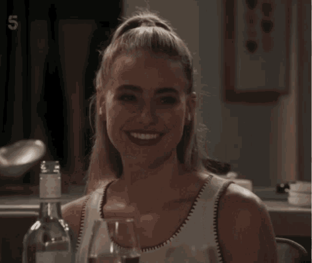 a woman sitting at a table with a bottle of water and a glass of wine with the number 5 on the bottom left