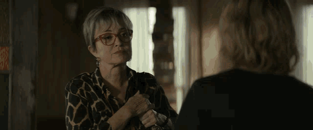 a woman wearing glasses talks to another woman in a dark room