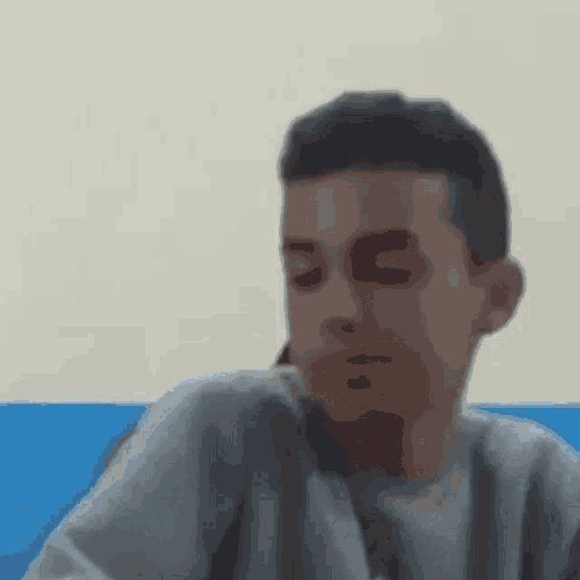 a young boy is sitting at a table with his eyes closed and looking at the camera .