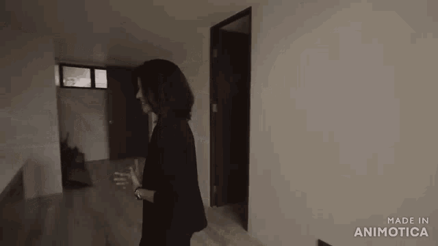 a woman in a black suit is standing in an empty room with the words made in animatica on the bottom