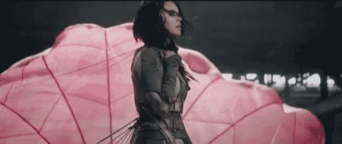 a woman in a futuristic outfit is standing in front of a large pink object .