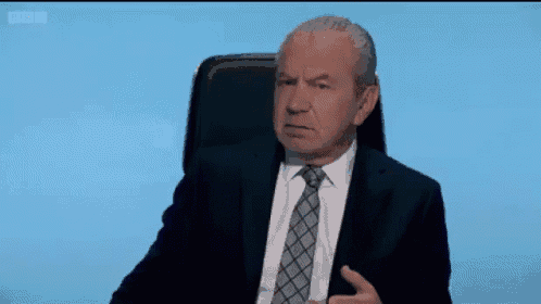 a man in a suit and tie is sitting in a chair and making a face .