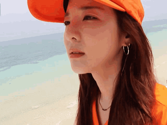 a woman wearing an orange hat and hoop earrings stands on a beach