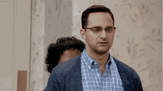 a man in a plaid shirt and glasses is standing next to another man in a room .