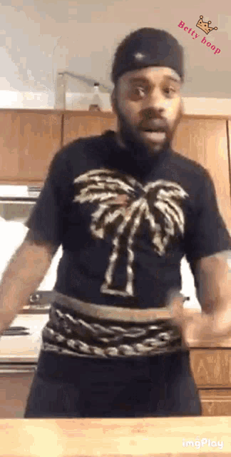 a man in a black shirt with a palm tree on it is dancing in a kitchen .