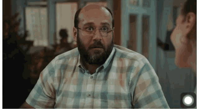 a man wearing glasses and a plaid shirt is talking to a woman