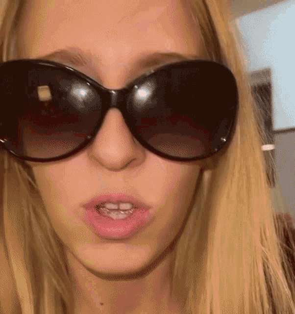 a close up of a woman wearing sunglasses and making a face