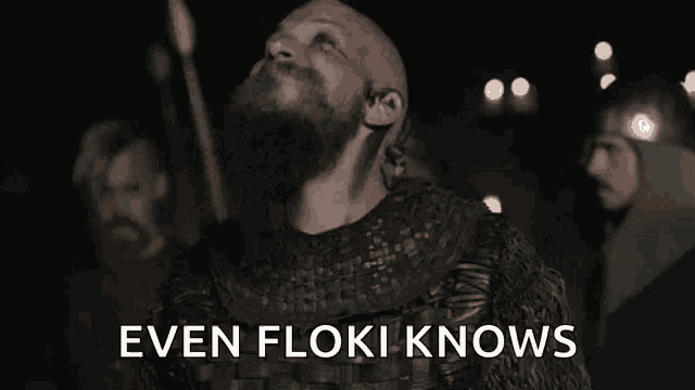 a man with a beard is standing in front of a group of men with the words even floki knows above him