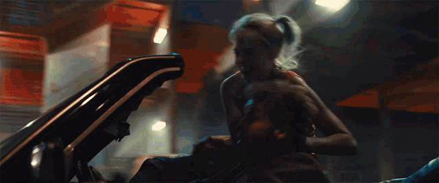 harley quinn is riding on the back of a man in a convertible car .