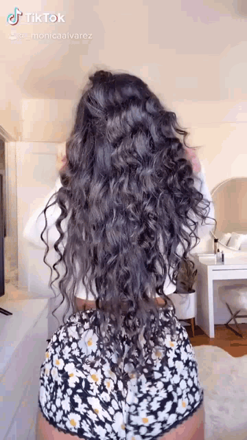 a woman with long curly hair is standing in a room wearing shorts and a white shirt .