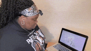 a woman wearing a headband is sitting in front of a laptop .