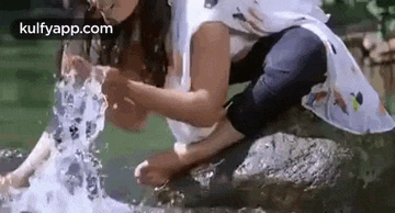 a woman is kneeling on a rock in front of a waterfall and splashing water on herself .