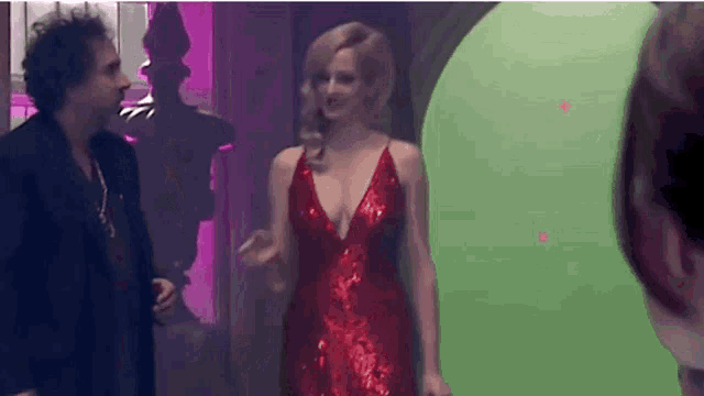 a woman in a red dress is standing in front of a green screen talking to a man .