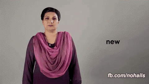 a woman wearing a pink scarf is standing in front of a grey background and says new .