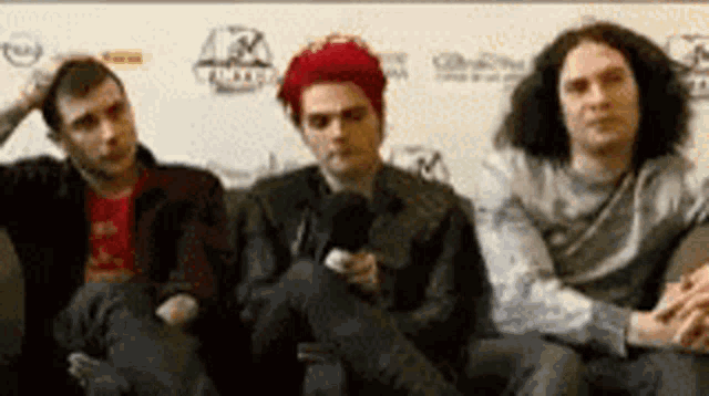 three men are sitting on a couch talking to each other .