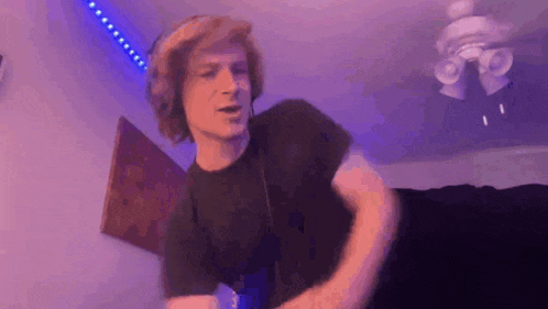 a man with red hair is dancing in a room with a ceiling fan and purple lights .