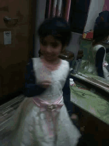 a girl in a white and pink dress is standing in front of a mirror