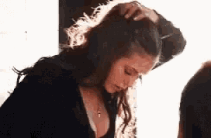 a woman is holding her hair in a ponytail while looking down .