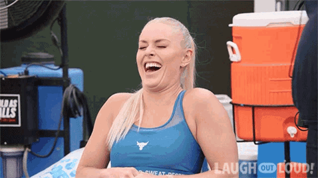 a woman in a blue tank top is laughing while sitting in front of an orange cooler .