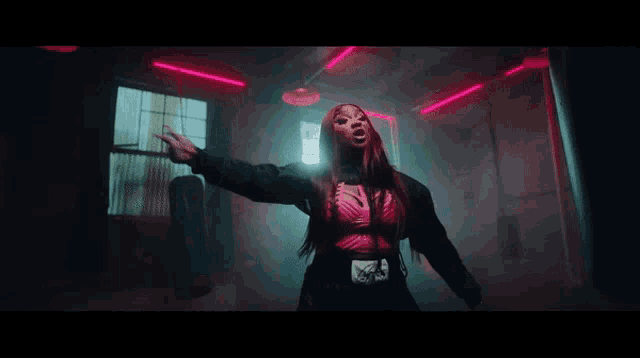 a woman in a pink top is standing in a dark room with red lights behind her